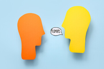 Paper human heads and speech bubble with word RUMORS on blue background. Gossip concept